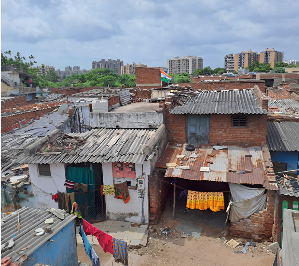 View of densely packed rooftops in a low-income urban neighborhood, with clothes hanging to dry and an Indian flag visible in the background