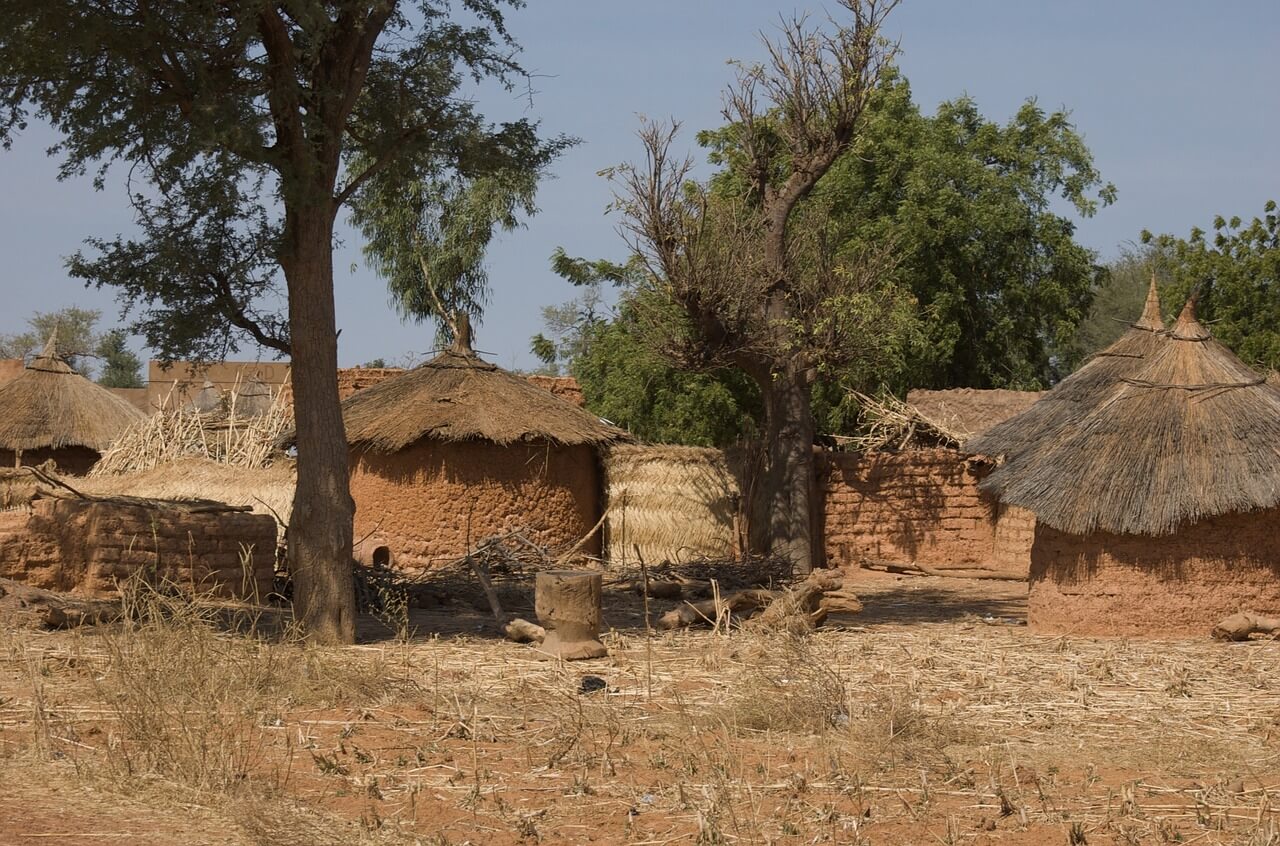Traditional rural huts with thatched roofs in a dry, sparsely vegetated African landscape.