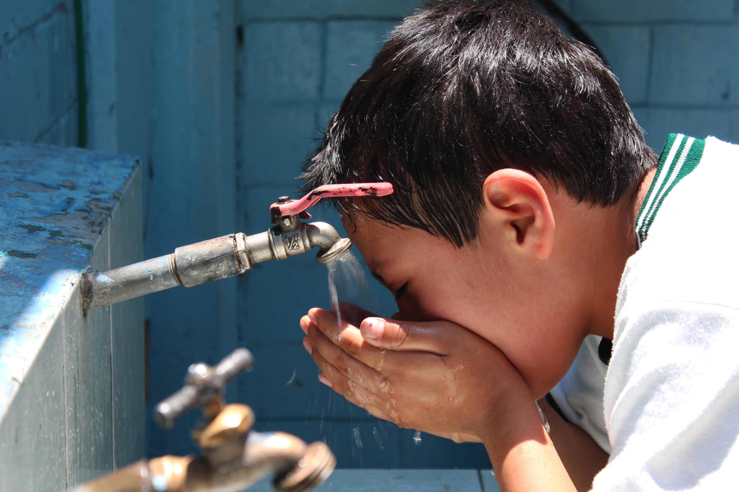 Young boy drinking water from a tap, using his hands to catch the flow