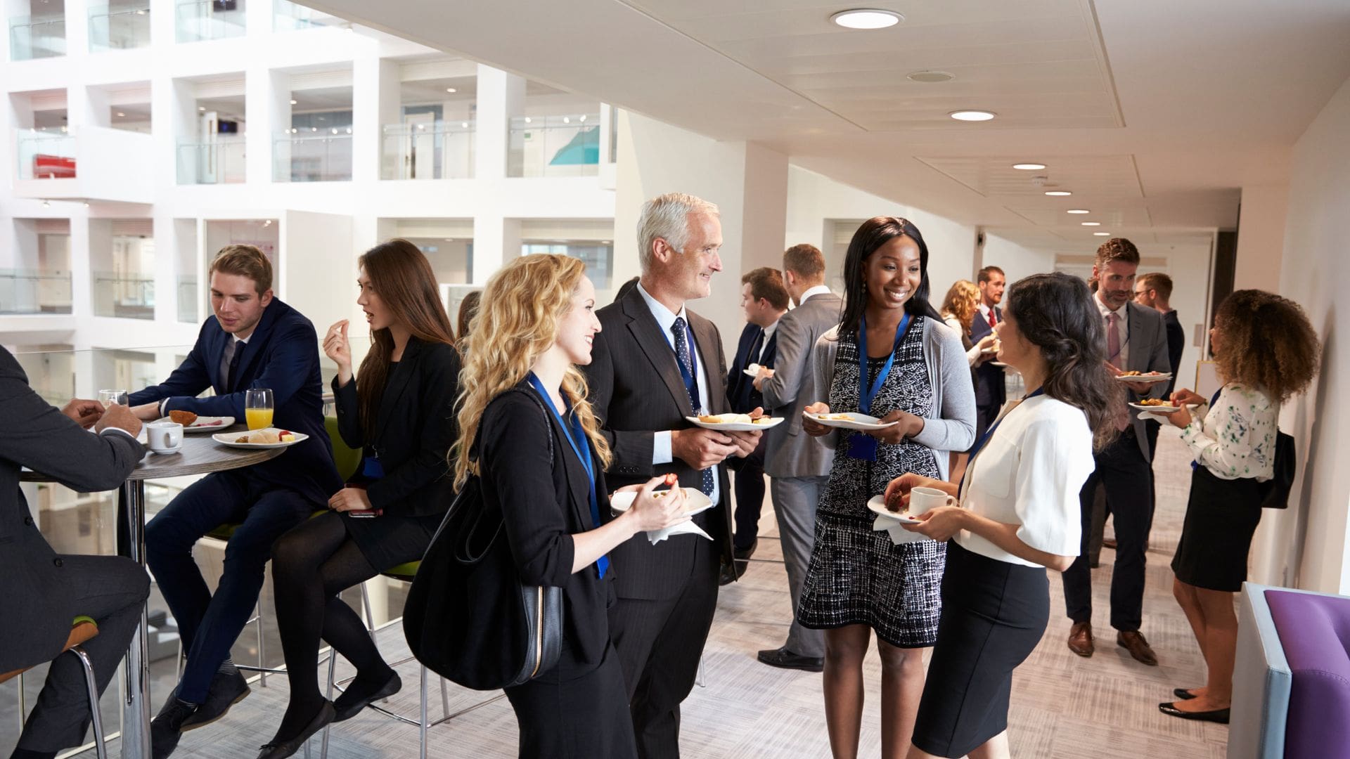 Professionals networking and conversing during a conference or summit break in a modern, bright venue.