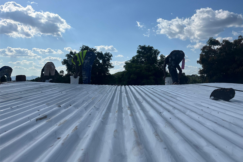 A photo of painters applying a white, heat repellent paint on a roof