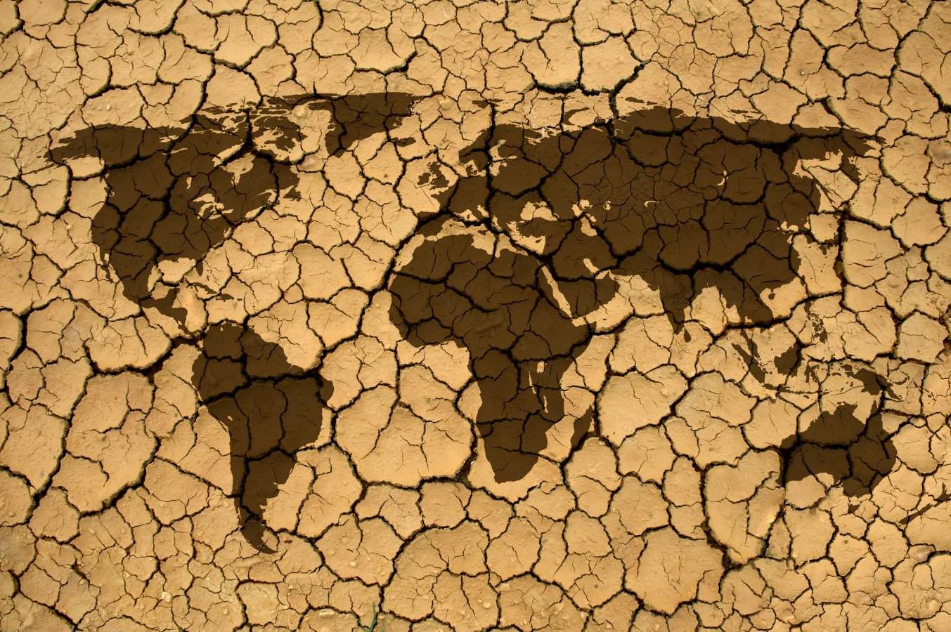 A world map illustration overlaid on cracked, dry earth, symbolizing global drought, climate change, and environmental degradation