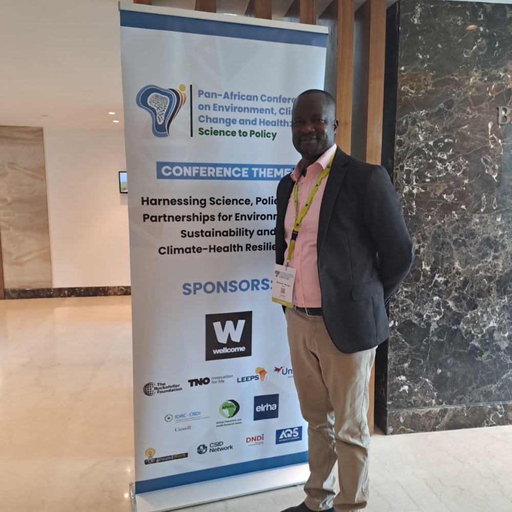 A photo of Dr. Bernard Abong'o, standing in front of a conference banner for the Pan-African Conference on Environment, Climate Change and Healthcare.