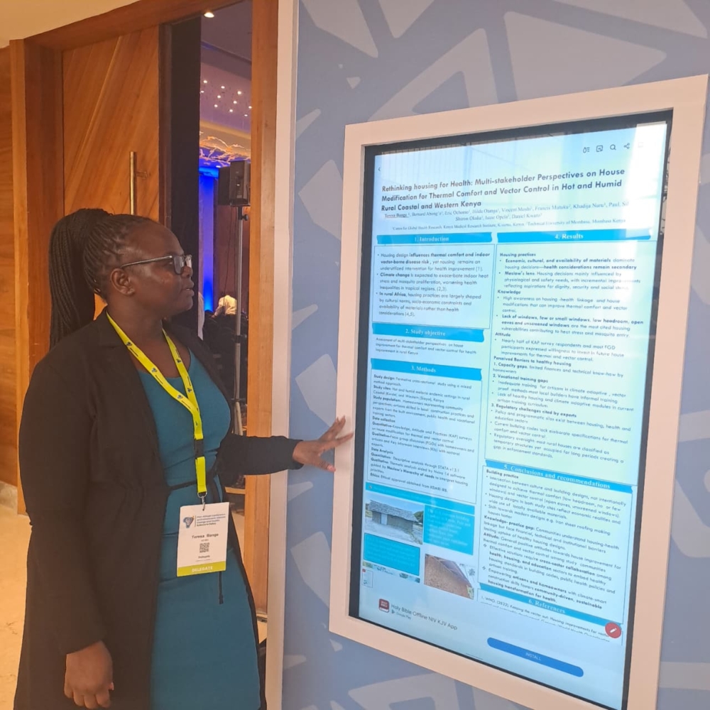 A photo of Teresa Bange,. standing next to a research poster and pointing at it.